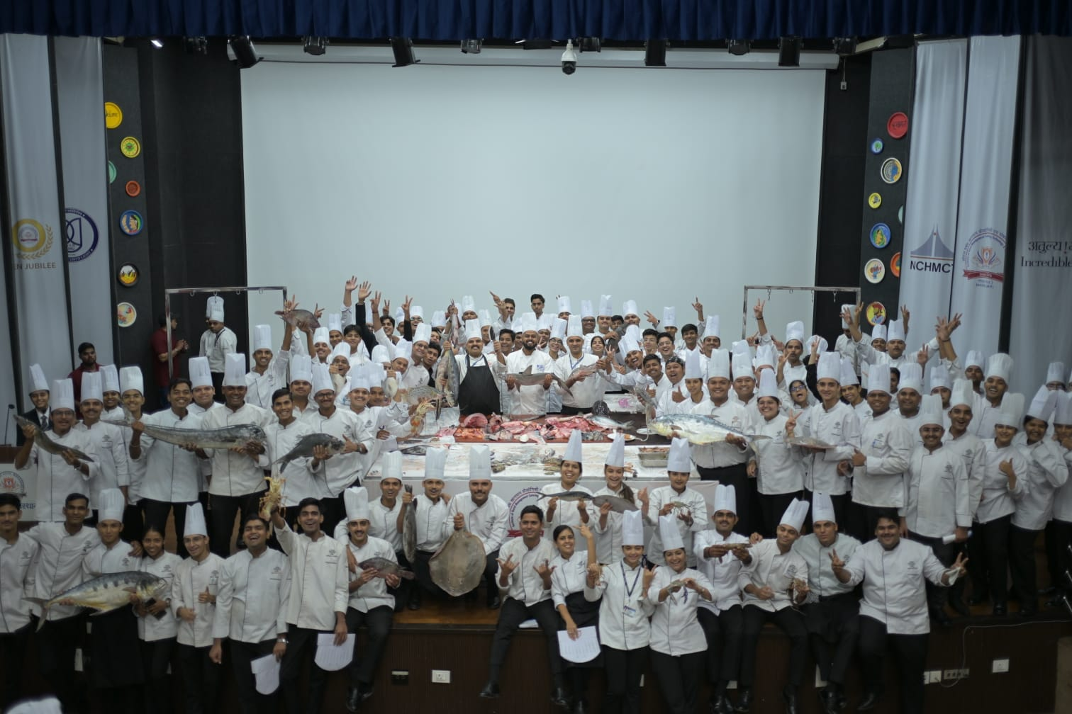Large group of hospitality students on stage holding fresh fish and seafood at the IHM Bhopal workshop
